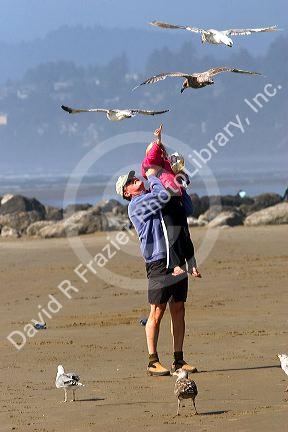 Father and daughter feeding gulls on the beach at Newport, Oregon.