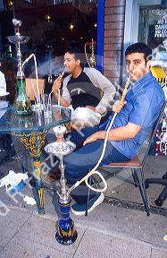 Turkish men smoking tobacco with a water pipe at a sidewalk cafe in London, England.