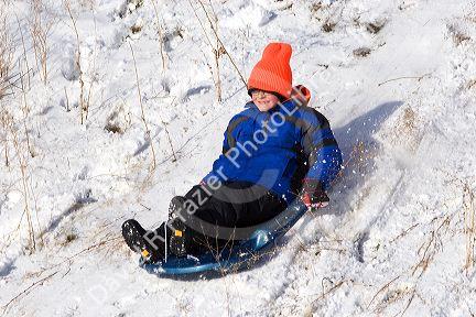 Boy sledding down a snow covered hill in Idaho. MR