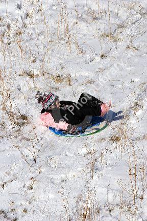 A young girl sledding on a snow covered hill in Idaho. MR