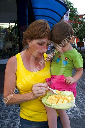 Mother and daughter eating a corn snack purchased from a street vendor in the Liberdade asian section of Sao Paulo, Brazil.