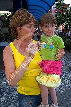 Mother and daughter eating a corn snack purchased from a street vendor in the Liberdade asian section of Sao Paulo, Brazil.
