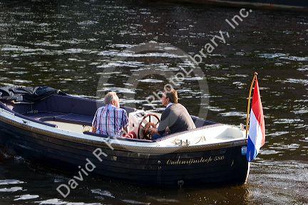 Men cruise in a canal boat on the Amstel River in Amsterdam, Netherlands.