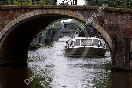 Canal boat traveling under a bridge on a canal near the Amstel River in Amsterdam, Netherlands.