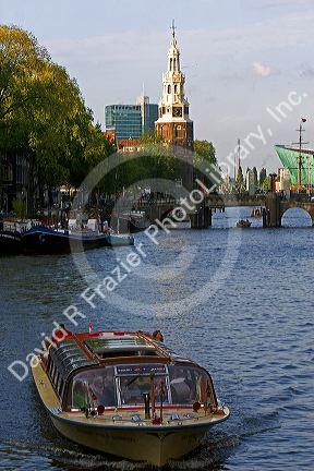 Canal boat on the Amstel River with Montelbaans Tower in the background, Amsterdam, Netherlands.