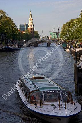 Canal boat on the Amstel River with the Montelbaans Tower in the background, Amsterdam, Netherlands.