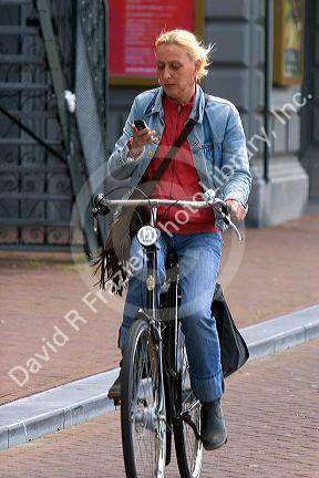 Woman using a cell phone while riding a bicycle in Amsterdam, Netherlands.