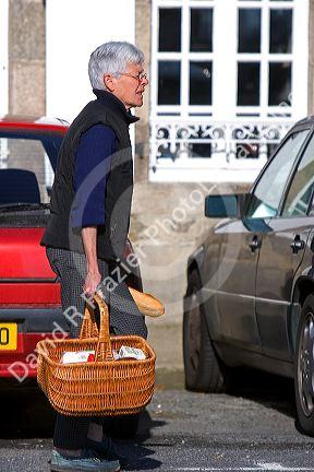 French woman walking with a shopping basket in the village of Barfleur in the region of Basse-Normandie, France.
