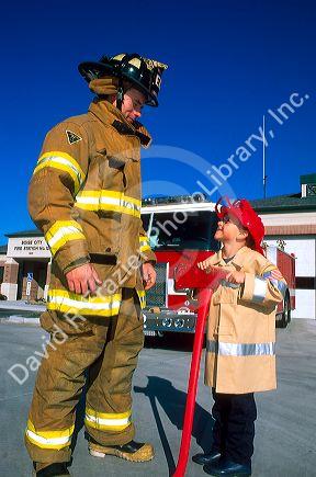 7 year old boy dressed in his home made Halloween costume as a firefighter, looks up to the real firefighter.