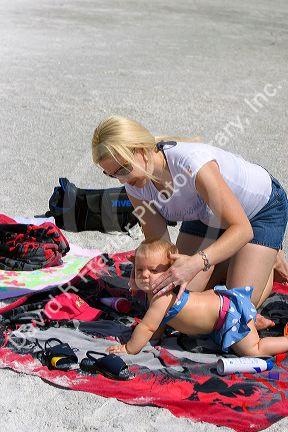 Mother applying sunscreen to her infant daughter at the beach in St. Petersburg, Florida. MR