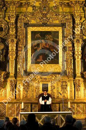 A priest performing mass in front of a gold alter inside the Catedral Metropolitana located on the central square, the zocalo, Mexico.