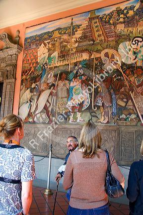 A tour guide showing tourists a mural painted by Diego Rivera at the National Palace in Mexico City, Mexico.