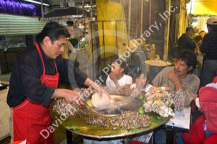 Vendor cooking cabeza tacos using a cazo at the Merced Market in Mexico City, Mexico.