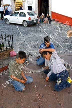 Mexican boys playing a game of pogs in the plaza at Taxco in the State of Guerrero, Mexico.