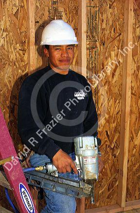 Hispanic construction worker wearing a hard hat and holding a pneumatic nail gun in Boise, Idaho. MR