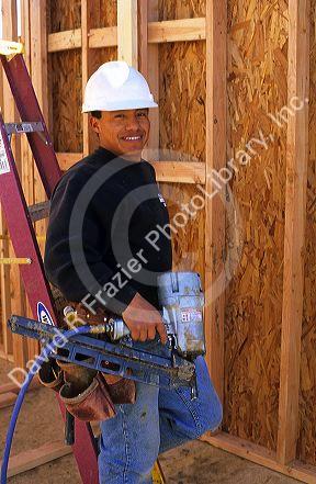 Hispanic construction worker wearing a hard hat and holding a pneumatic nail gun in Boise, Idaho. MR