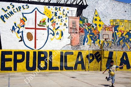Young boy playing soccer in front of a mural in the La Boca barrio of Buenos Aires, Argentina.