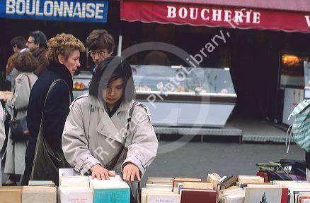 Woman looking through books at an outdoor market in Paris, France.