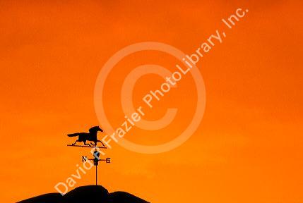 weathervane atop barn at sunset indicates wind direction.