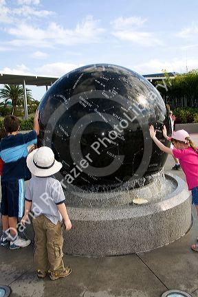 Children push the Constellation Sphere, a 9 ton granite sphere floating on water at the Kennedy Space Center Visitor Complex in Cape Canaveral, Florida.