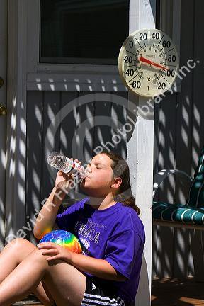 11 year old girl drinking water below a thermometer reading 100 degrees fahrenheit on a hot summer day in Boise, Idaho. MR