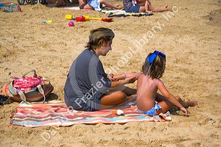 Mother applying sunscreen to her daughter on the beach at La Concha Bay in the city of Donostia-San Sebastian, Guipuzcoa, Basque Country, Northern Spain.