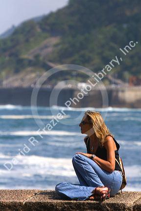 Woman sits on a seawall in the city of Donostia-San Sebastian, Guipuzcoa, Basque Country, Northern Spain.
