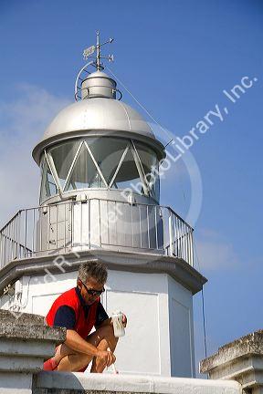 Man painting a lighthouse in the town of Llanes, Asturias, Spain.