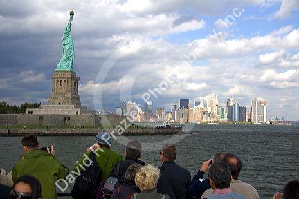 Tourists view the Statue of Liberty and Lower Manhattan from New York Harbor, New York, USA.