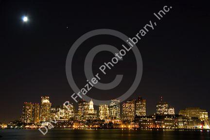 Boston skyline on a moonlight starry night with Boston Harbor in the foreground, Massachusetts, USA.