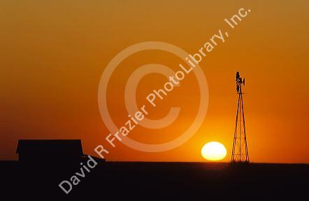 Windmill and barn silhouetted at sunset on farmland in western Kansas.
