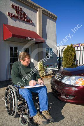 Handicapped insurance claims adjuster assessing the damage of an automobile in Boise, Idaho, USA. MR