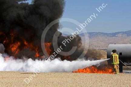 Firefighter using fire retardant foam to put out a jet fuel fire at an airport training facility in Boise, Idaho, USA.
