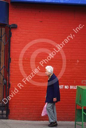 An elderly woman walks in front of a red brick wall in Chinatown, San Francisco, California.