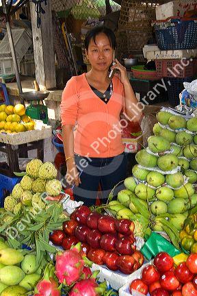 Vendor selling produce and speaking on a cell phone at a market in the Cholon district of Ho Chi Minh City, Vietnam.