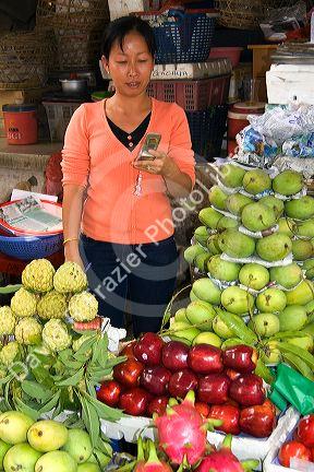 Vendor selling produce and using a cell phone at a market in the Cholon district of Ho Chi Minh City, Vietnam.