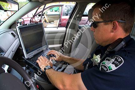 Police officer using a mobile data terminal computer inside a police car in Boise, Idaho, USA.