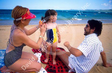 A hispanic family at the beach in Puerto Rico.  Mother is applying sun block on the daughter.