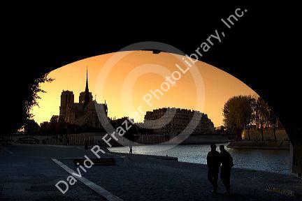 View of the Notre Dame cathedral at sunset through the arch of the Tournelle Bridge on the River Seine in Paris, France.