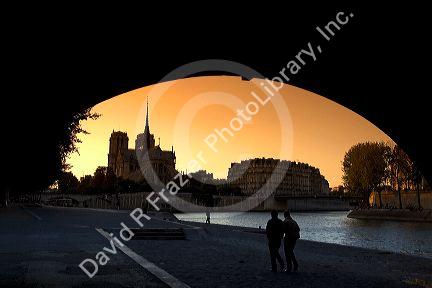 View of the Notre Dame cathedral at sunset through the arch of the Tournelle Bridge on the River Seine in Paris, France.
