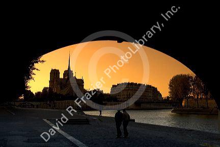 View of the Notre Dame cathedral at sunset through the arch of the Tournelle Bridge on the River Seine in Paris, France.