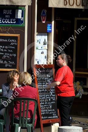 Waitress greeting customers at a sidewalk cafe in Paris, France.