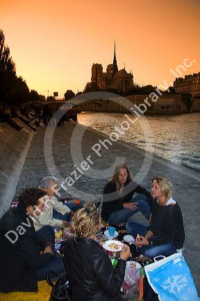 Parisiens picnicing along the River Seine at sunset in Paris, France.