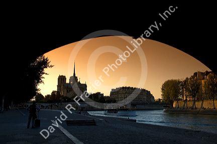 View of the Notre Dame cathedral at sunset through the arch of the Tournelle Bridge on the River Seine in Paris, France.