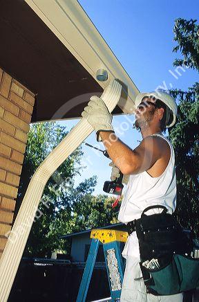 Worker putting on gutters and downspouts on a house.