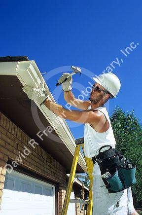 Worker putting on gutters and downspouts on a house.