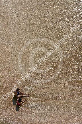 Mother and daughter sit on the beach in the surf at Acapulco, Guerrero, Mexico.