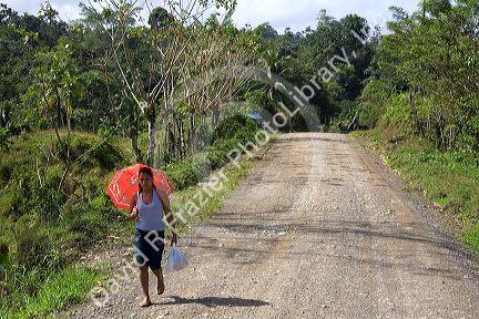 Costa Rican woman using an umbrella for shade, walking on a rural dirt road near Limon, Costa Rica.