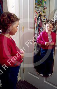 Five-year-old girl getting dressed, looking at herself in the mirror.