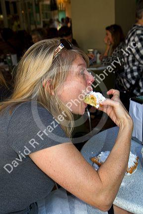 Woman eating a beignet at Cafe Du Monde in the French Quarter of New Orleans, Louisiana, USA.